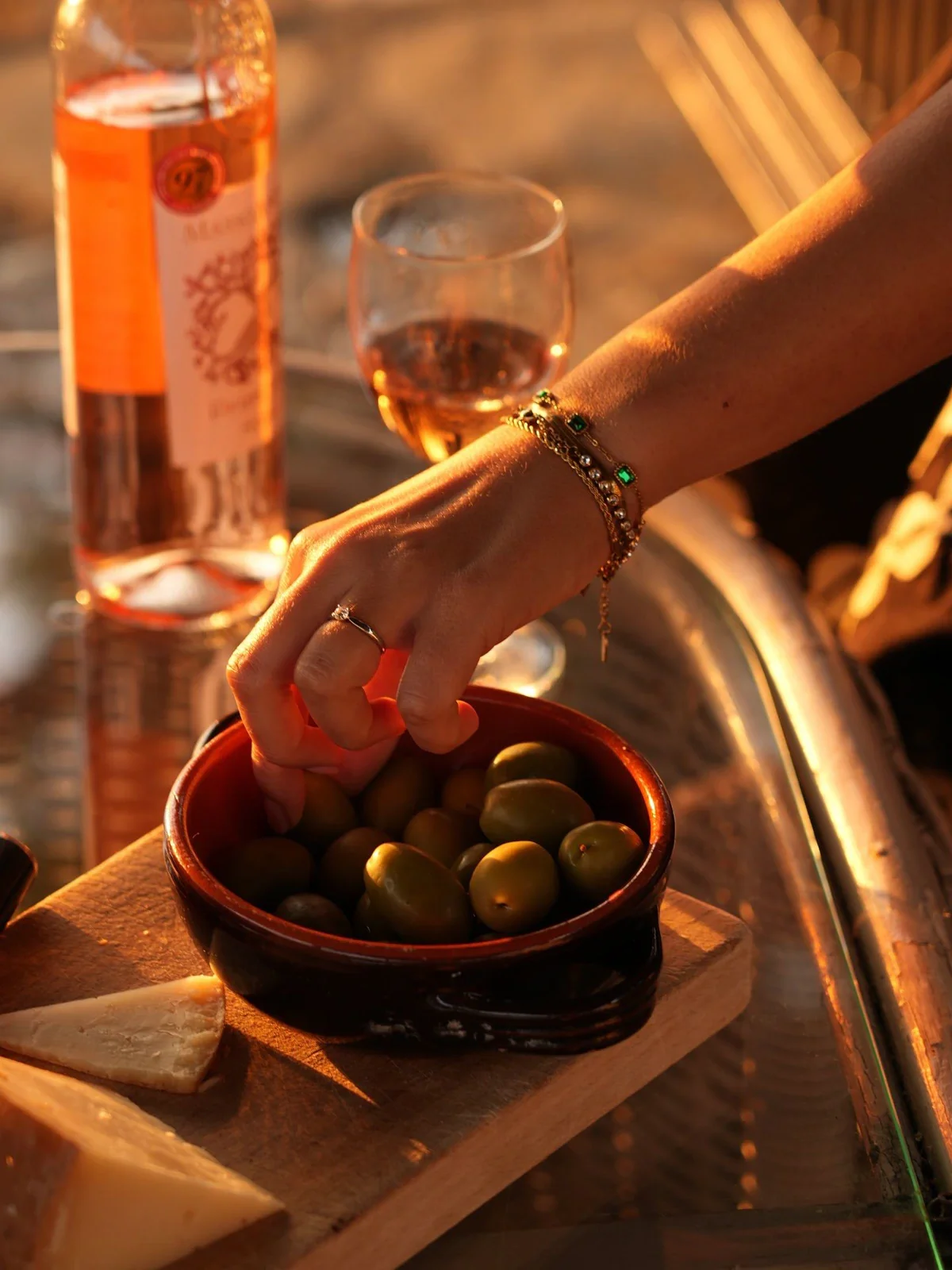 Charcuterie board with olives, cheese, and a glass of rosé on an outdoor table at golden hour