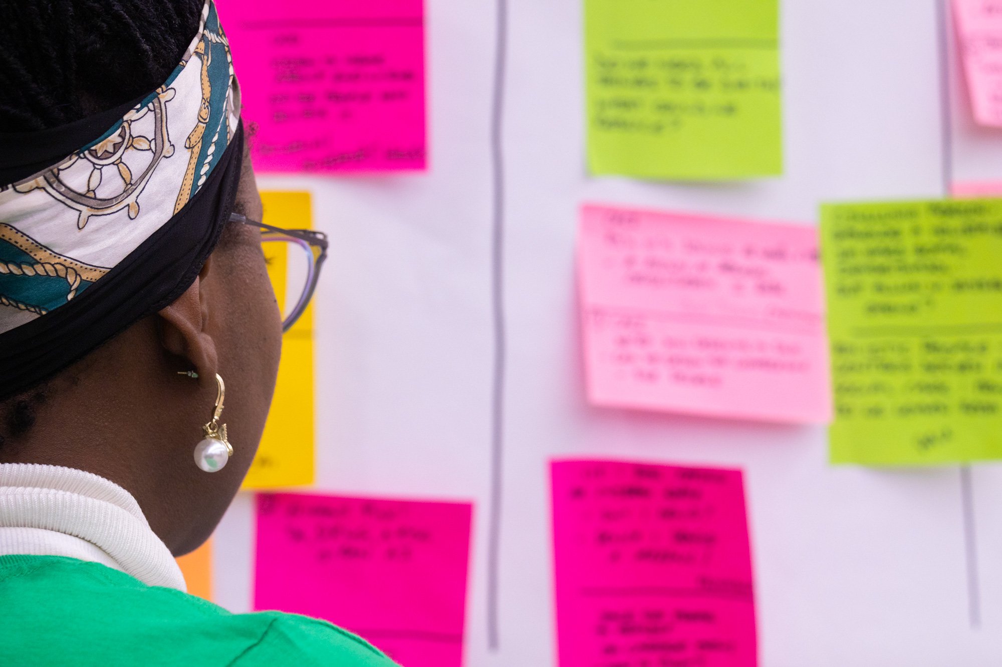 Woman with dark hair and headband looking at wall of post its