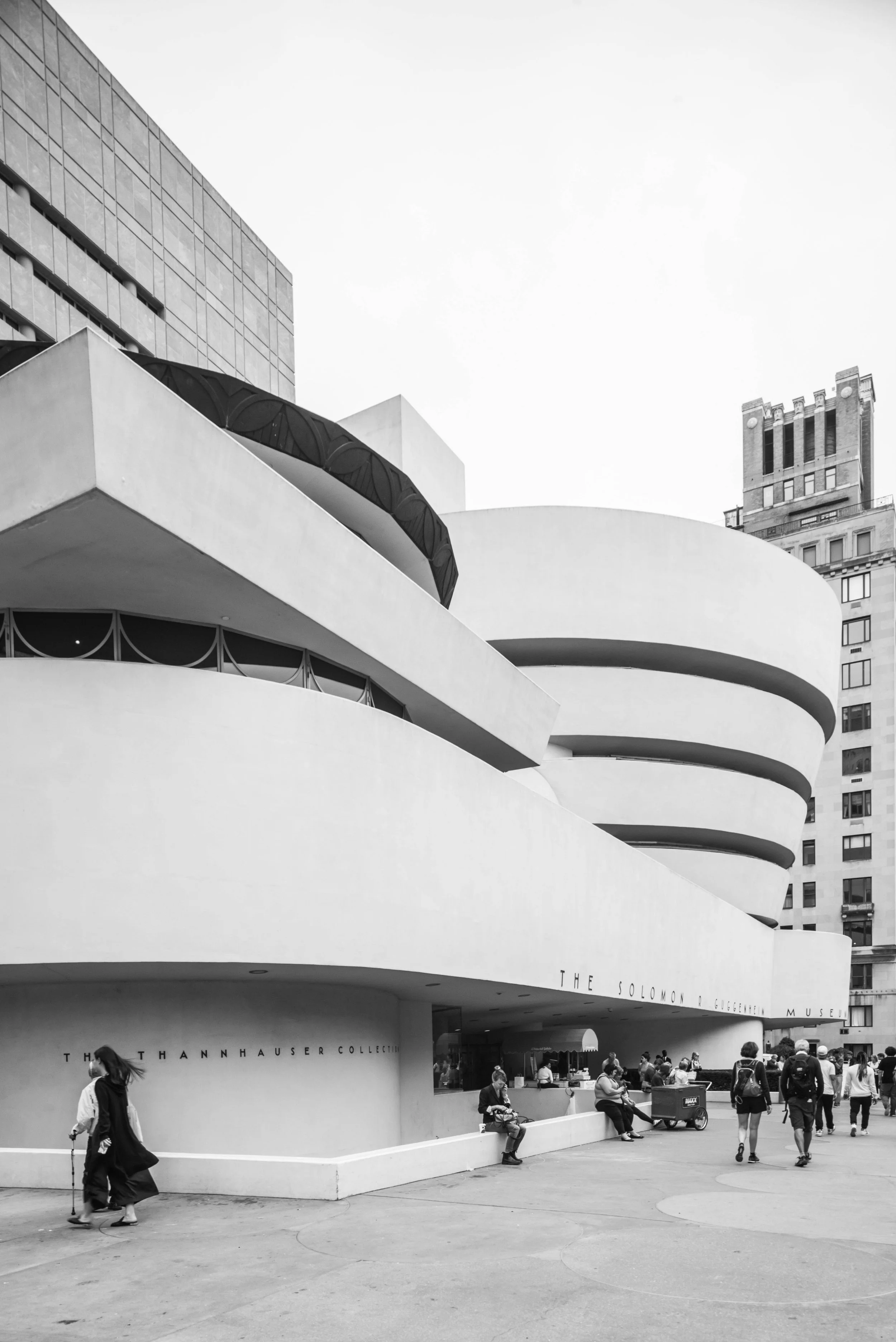 Imagen en blanco y negro del Museo Solomon R. Guggenheim en Nueva York con personas sentadas y caminando en el exterior.