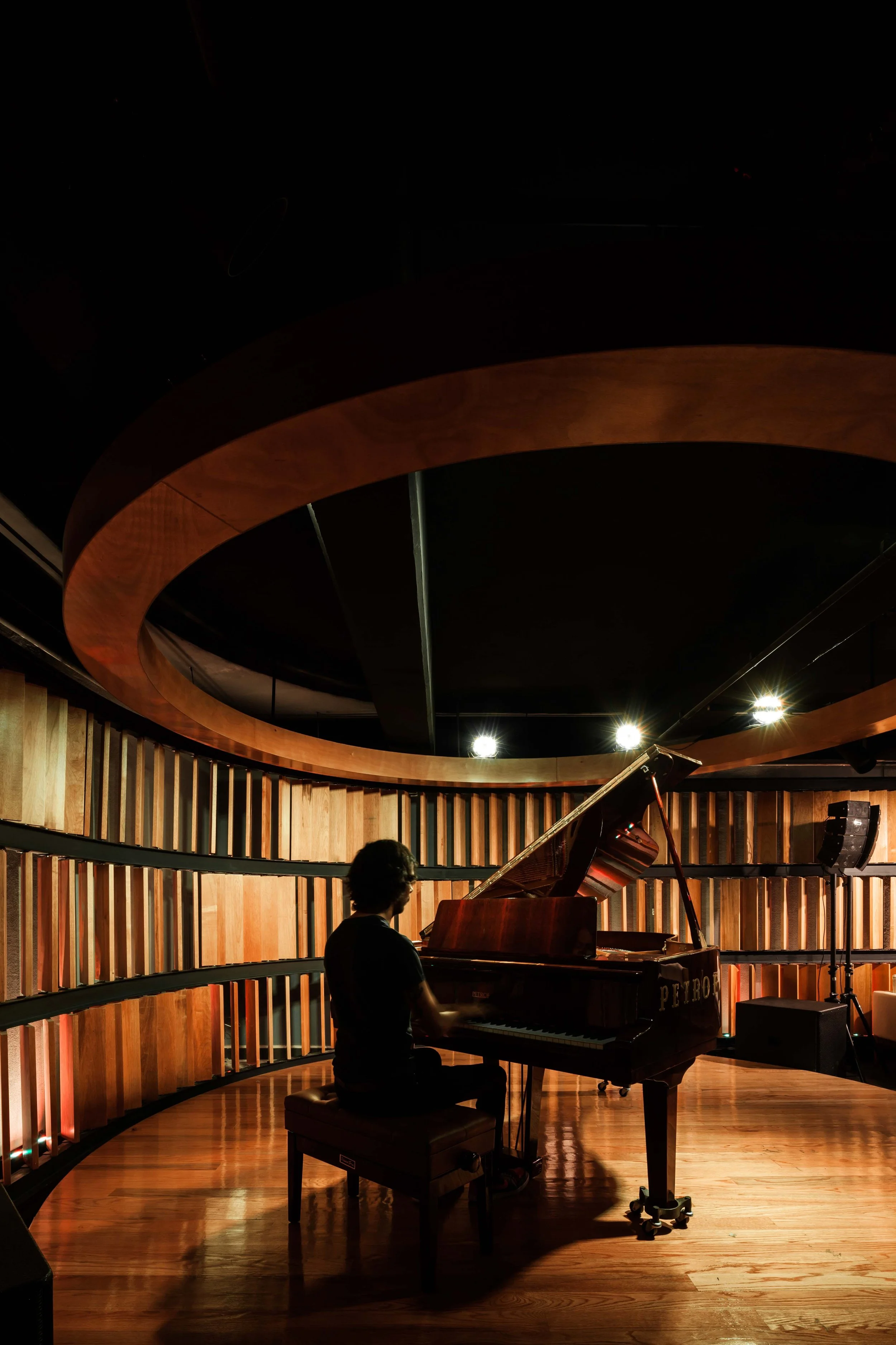 Persona tocando el piano en un escenario con paredes de madera y luces brillantes.