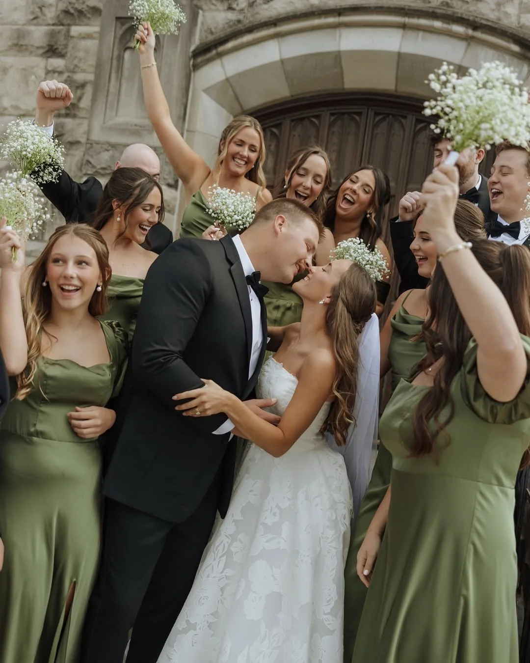 Bride and Groom kissing on Church steps after their ceremony surrounded by wedding party cheering