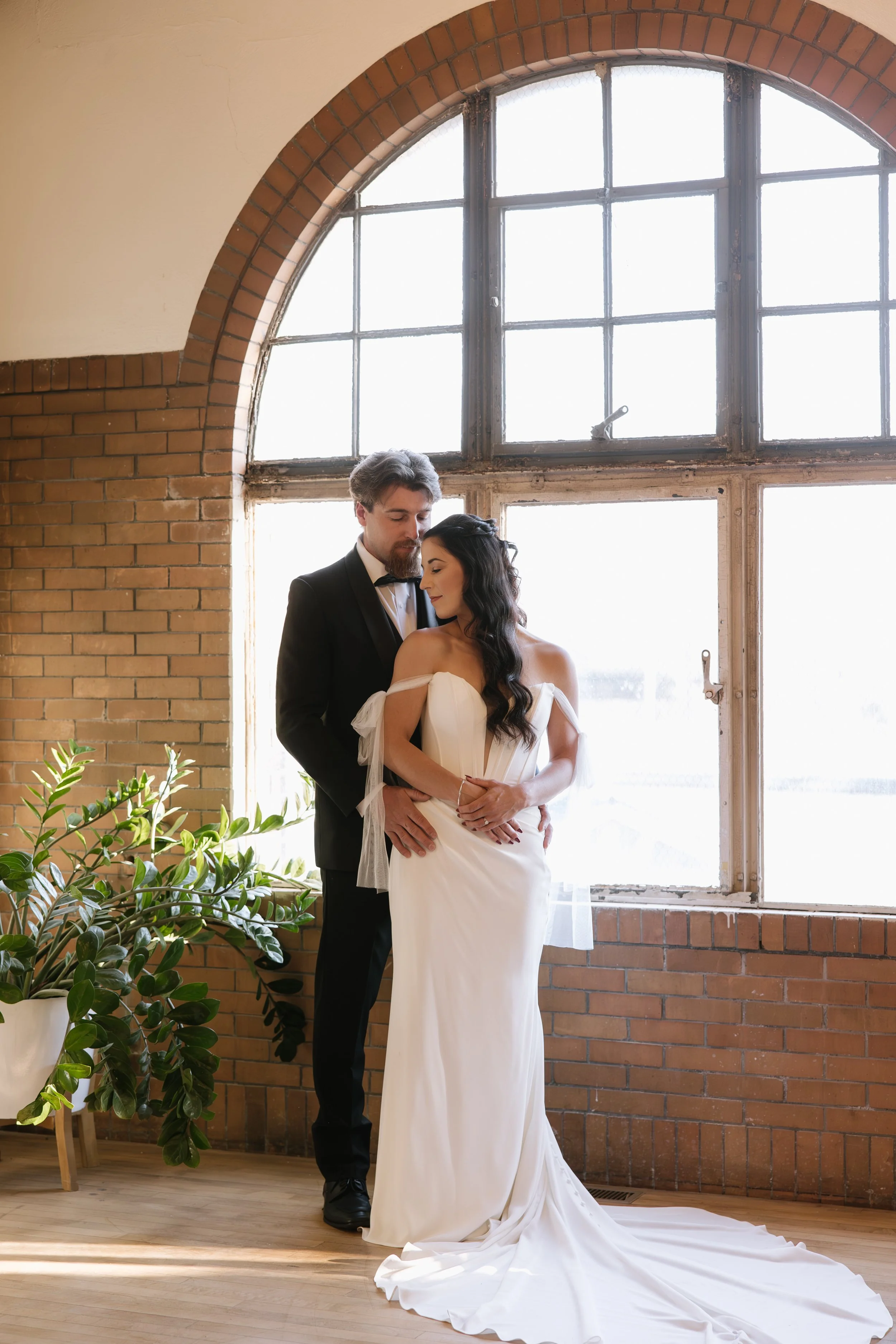 Bride & Groom Standing in front of a brick wall with a large window