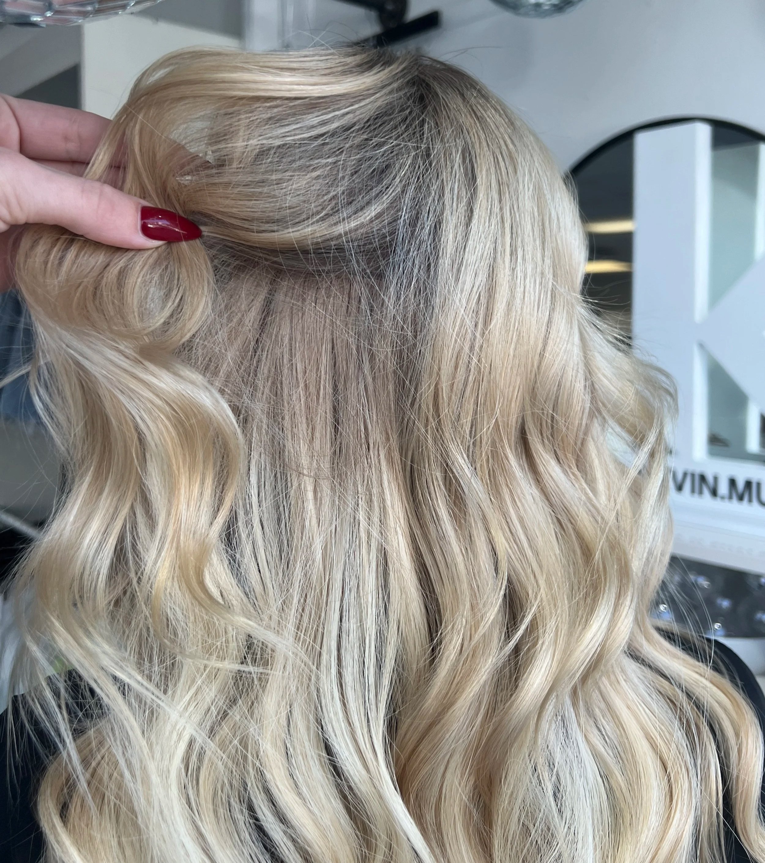 Close-up of blonde, wavy hair with a person's hand holding a section of the hair, showcasing the hair's texture and color.