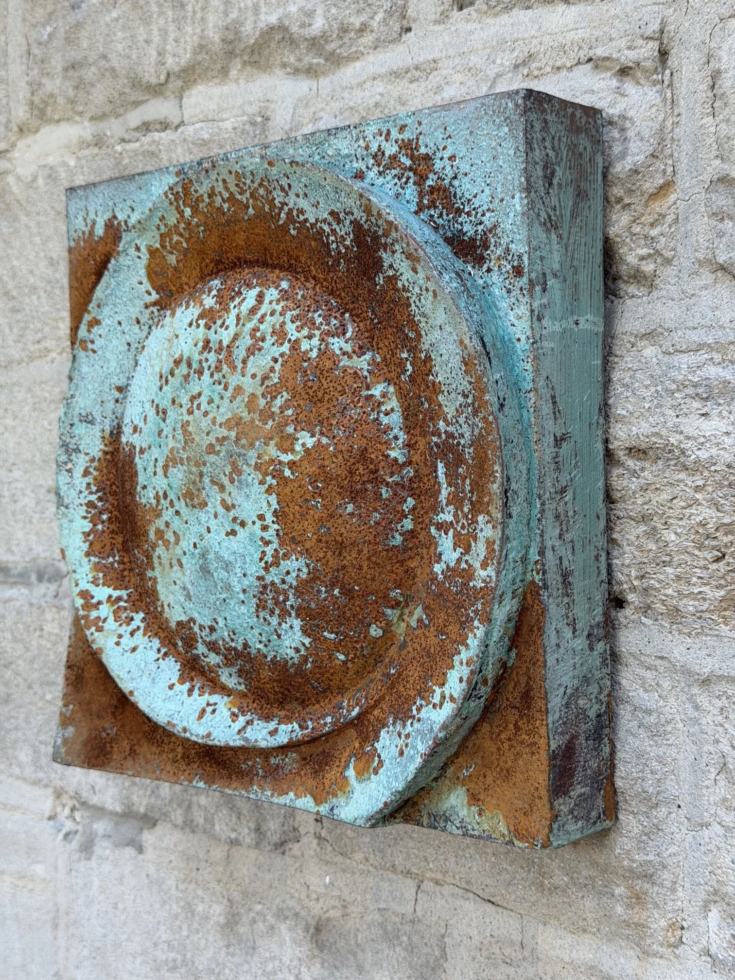 Moon Crater Phase Blue Wall Sculpture on a stone wall, its rust and turquoise disc catching the light