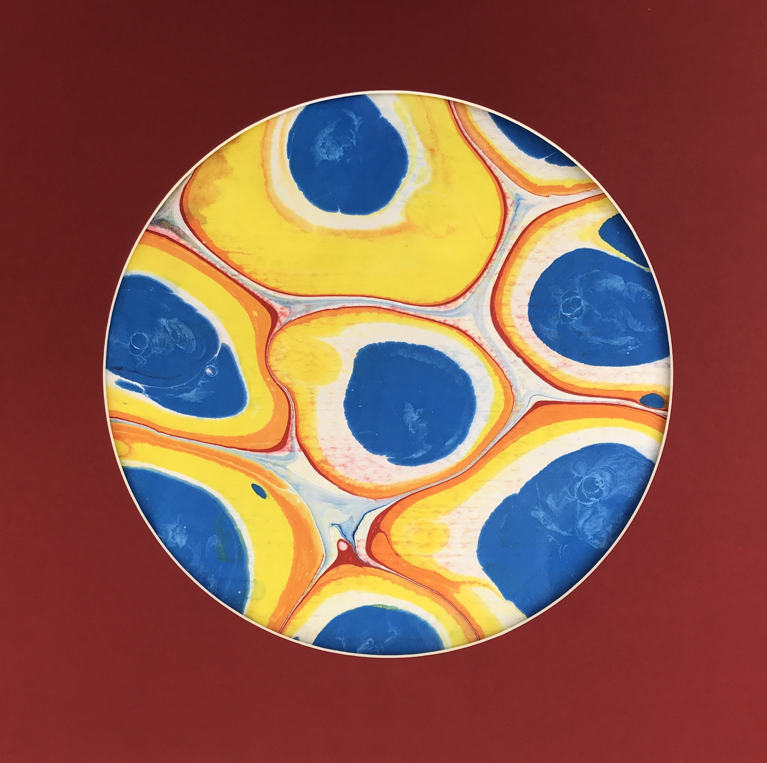 Globule Marbled Moon print, a circular disc of blue pools ringed in yellow and red marbling, on deep red