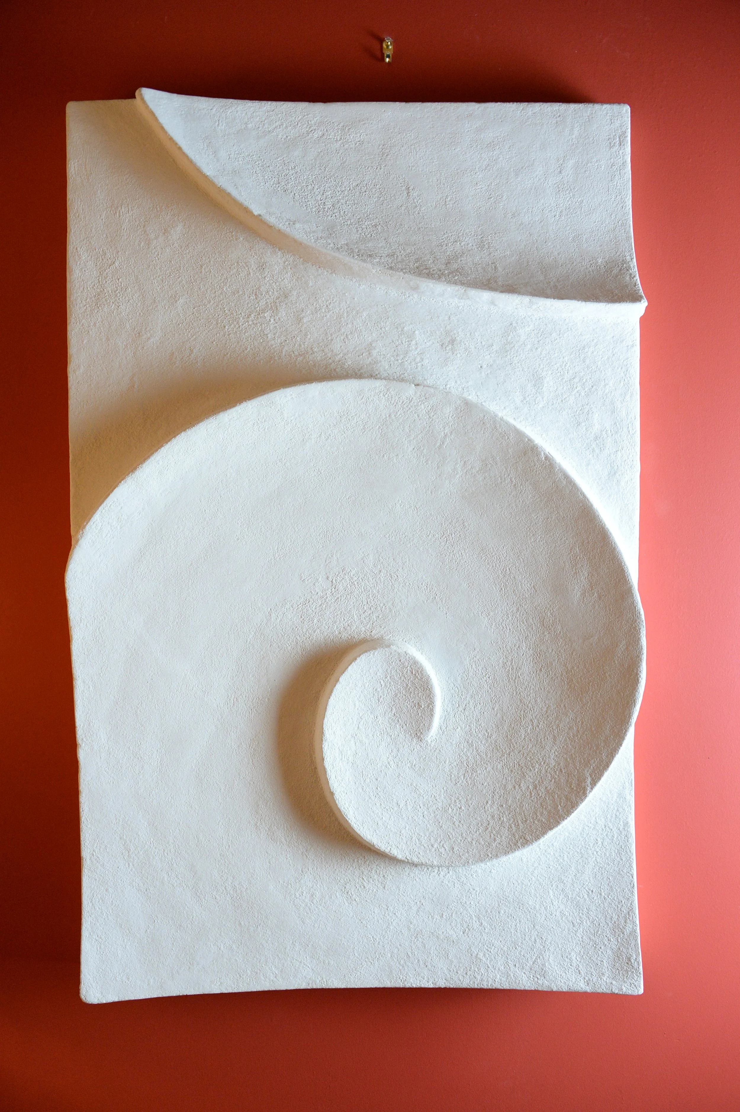 Moonwave wall sculpture in a white stone finish hung against a warm terracotta ground