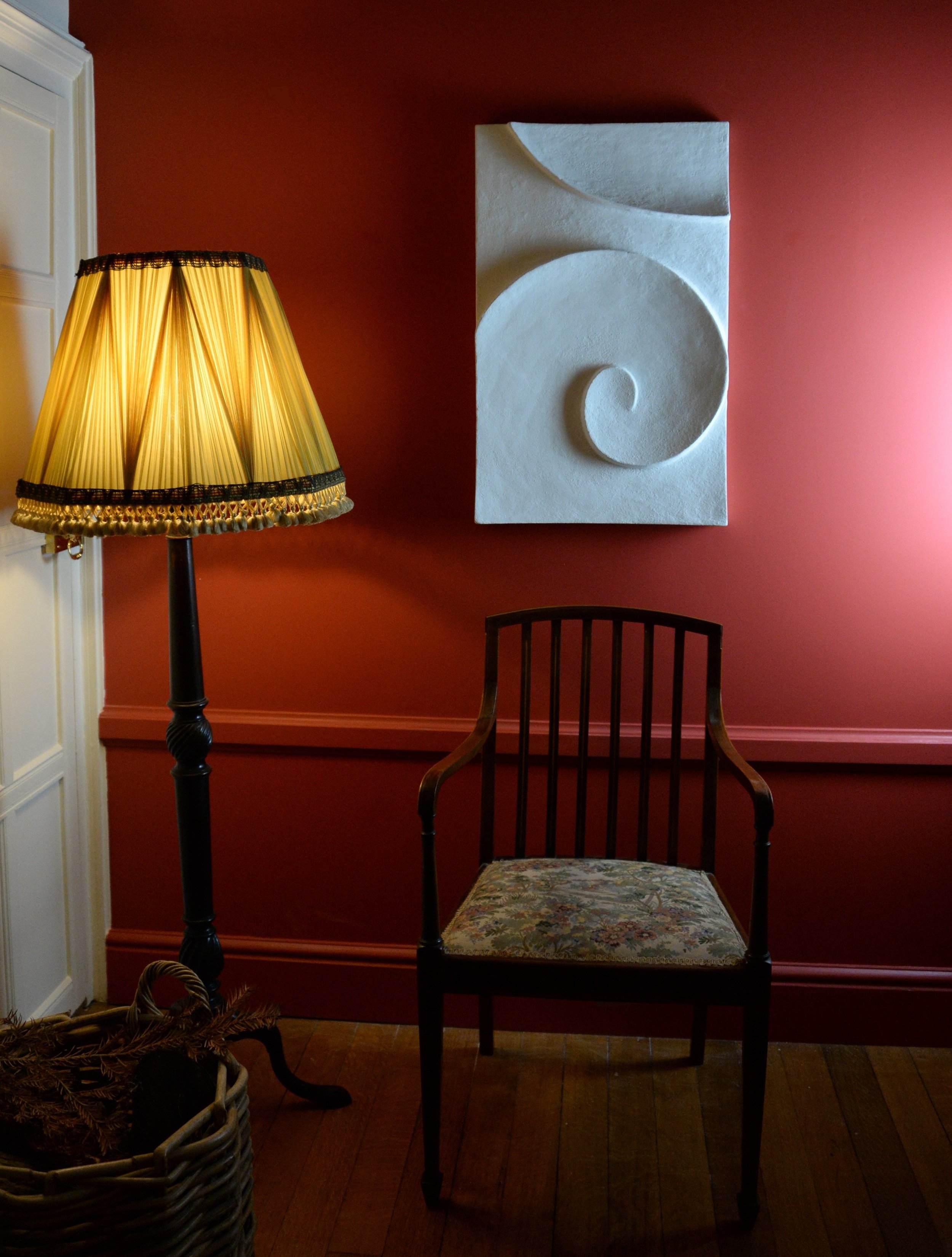 Moonwave wall sculpture on a deep red interior wall beside a table lamp and spindle-back chair