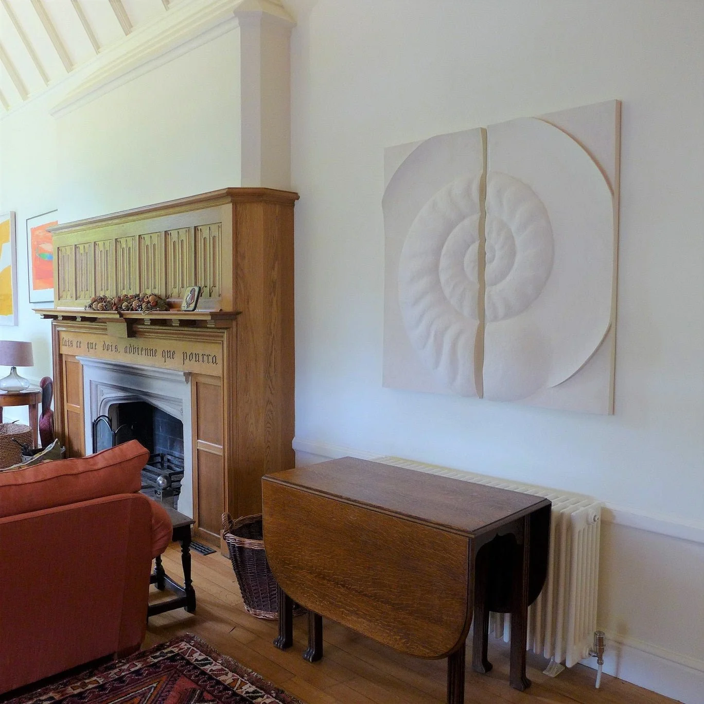Ancient Ammonite wall sculpture hung above a fireplace in a sitting room with a piano and armchair