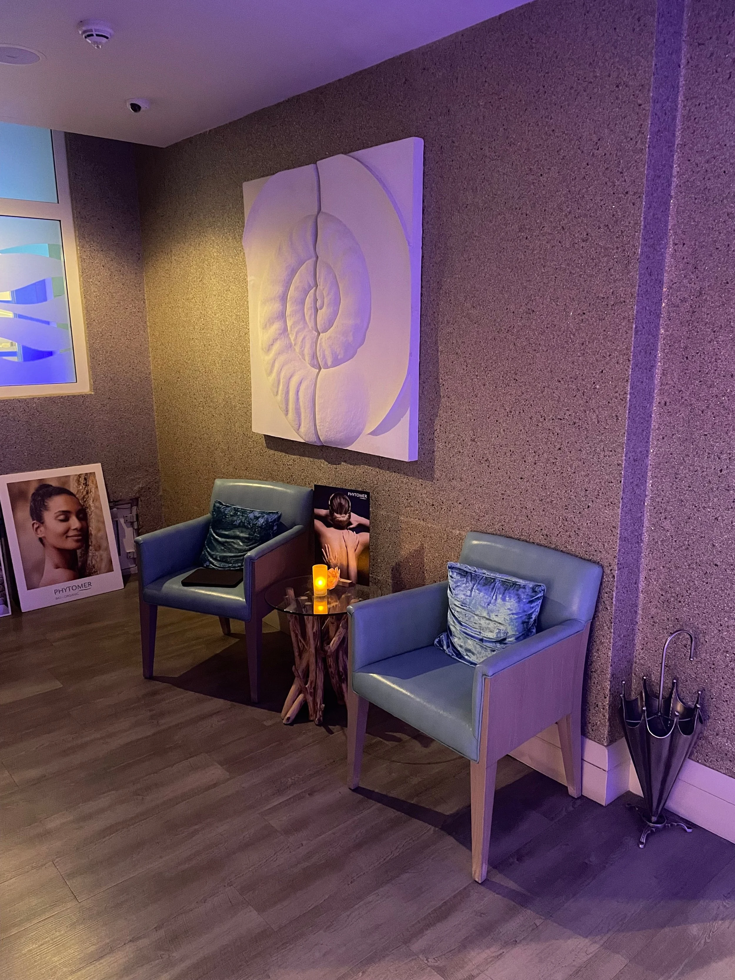 Ancient Ammonite wall sculpture lit in violet light in a treatment room with armchairs