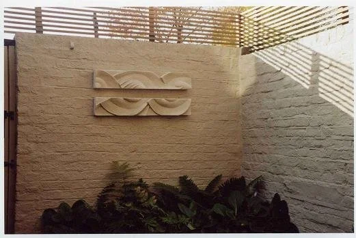 Two Frozen Decowaves wall sculpture on a rendered garden wall above a raised bed of planting