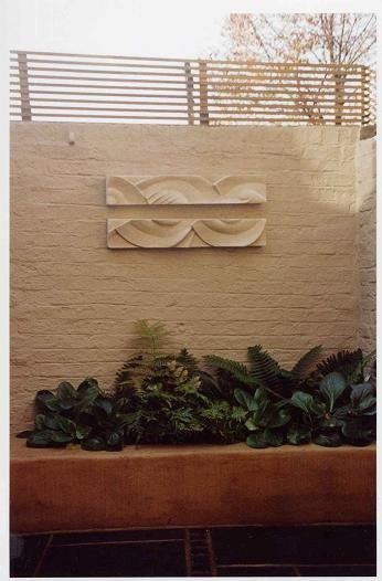 Two Frozen Decowaves wall sculpture on a garden wall above a terracotta trough, seen from further back