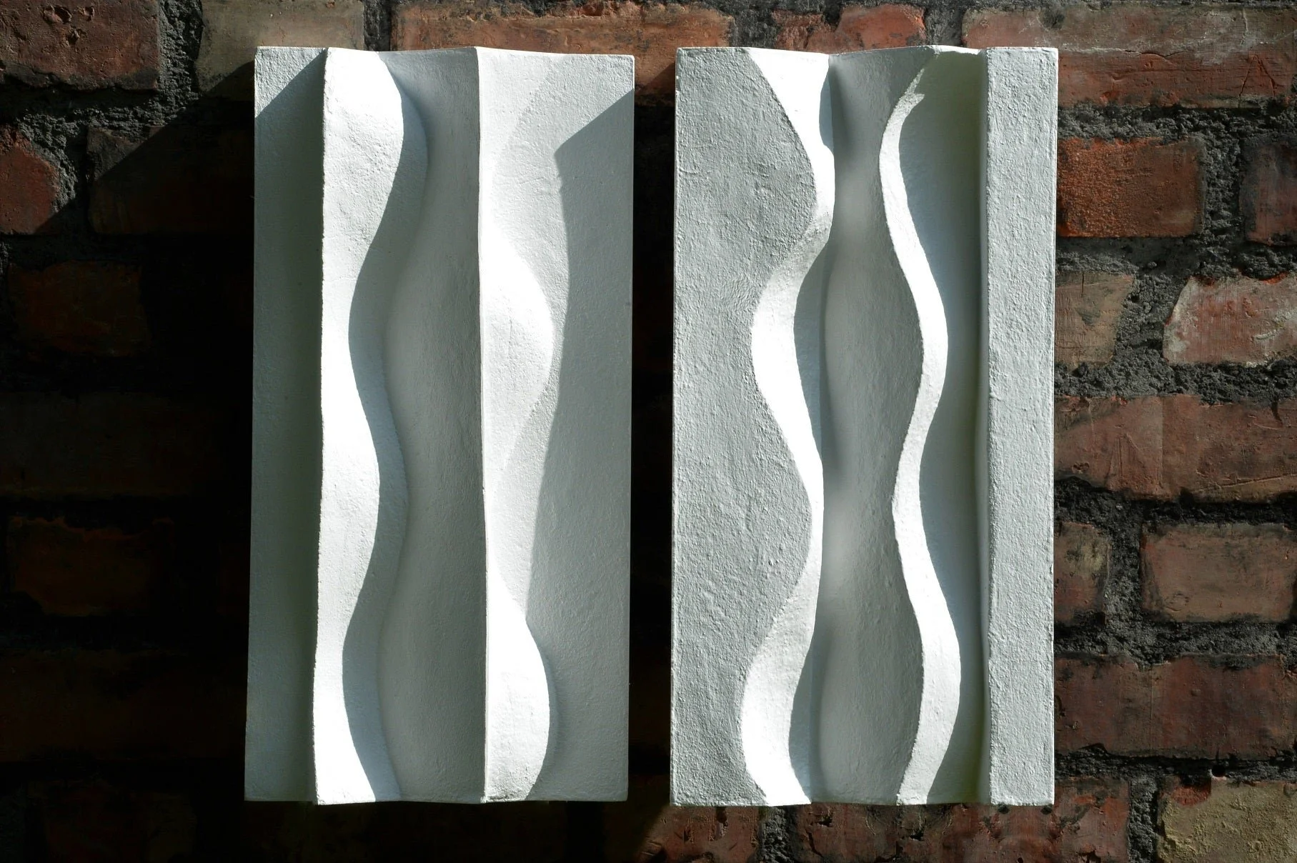 Brancusi wall sculpture, a pair of carved undulating panels mounted side by side on dark brick