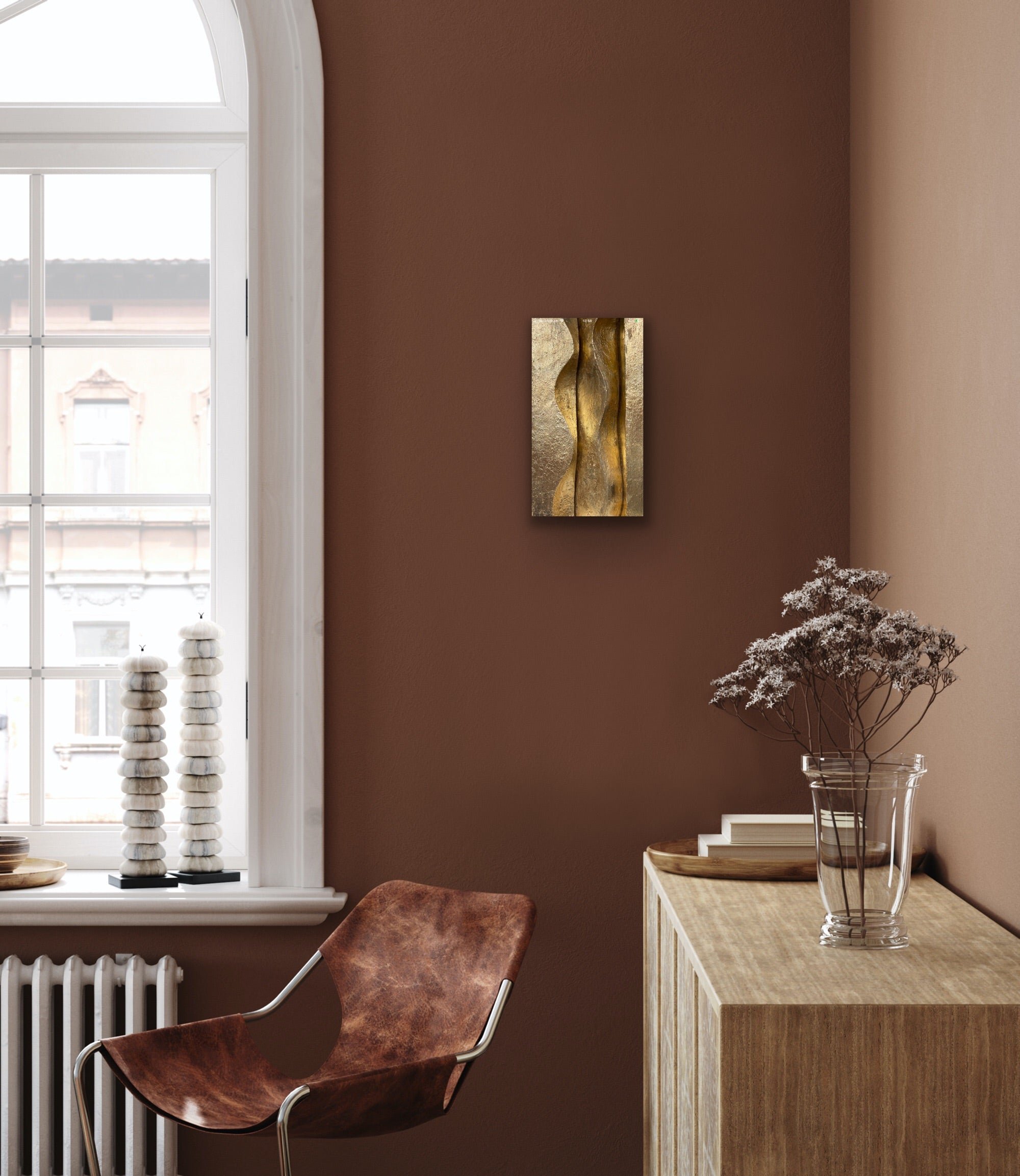 Brancusi wall sculpture in a gilded finish hung on a terracotta wall above a console table and leather chair