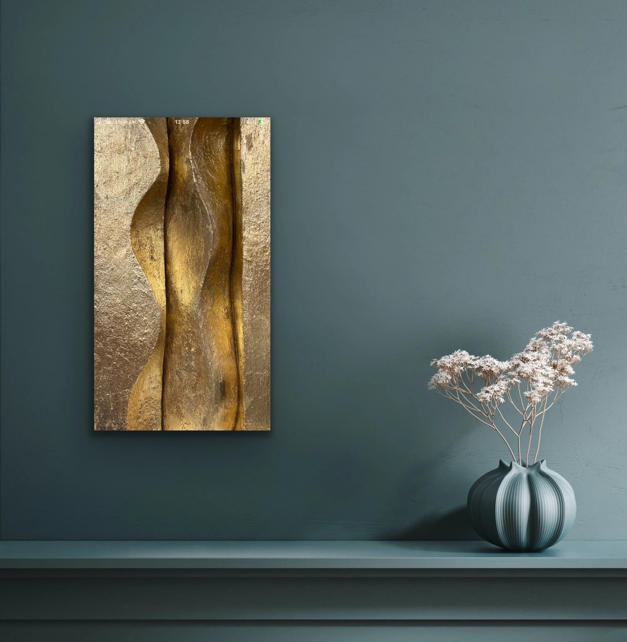 Brancusi wall sculpture in a gilded finish on a slate blue wall above a shelf with a vase of dried flowers