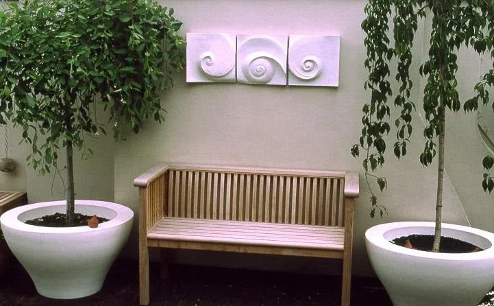 Moonphases Three wall sculpture above a timber bench between two clipped standard trees in planters