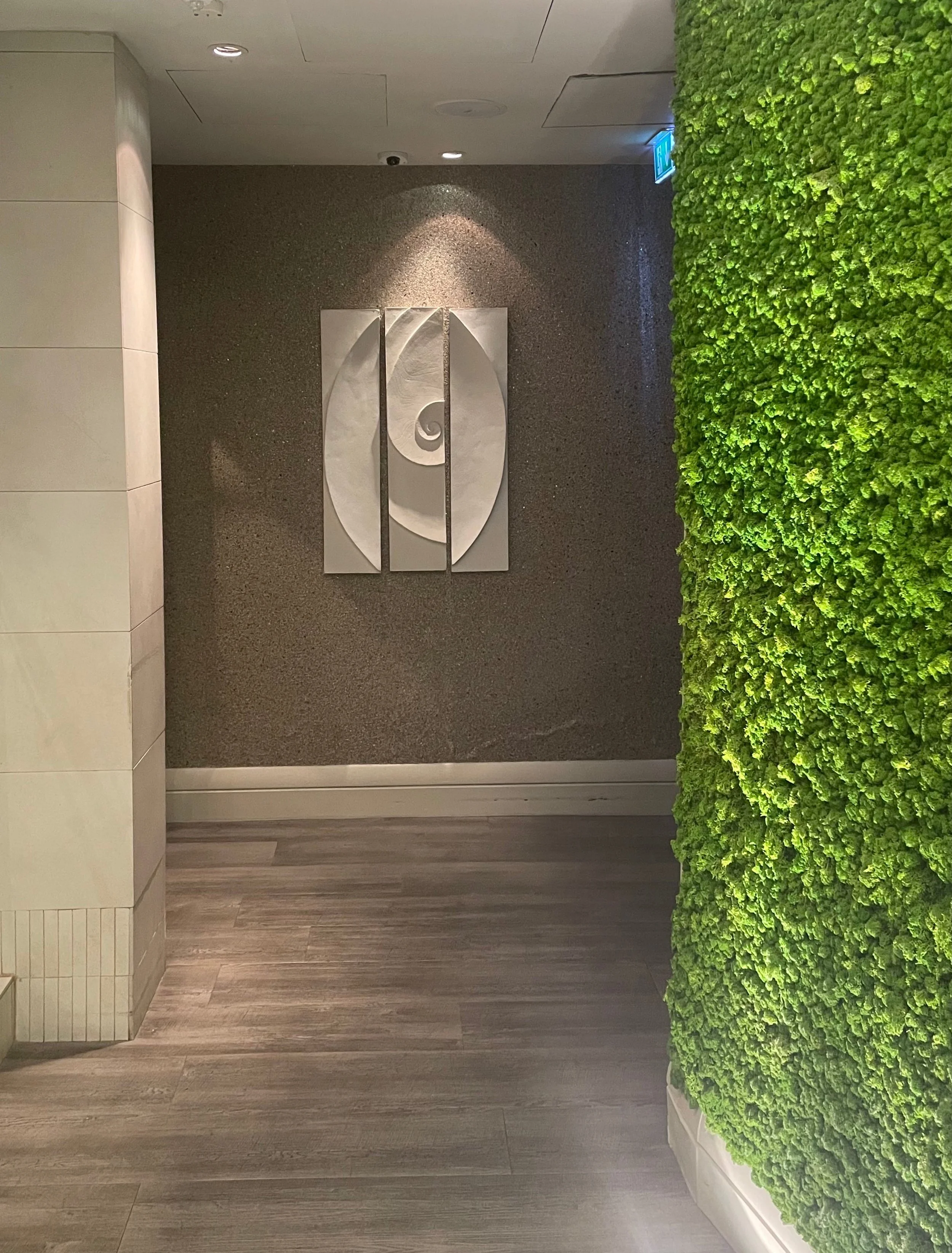 Shellwave Between Two Concave Moons wall sculpture in a corridor beside a living moss wall