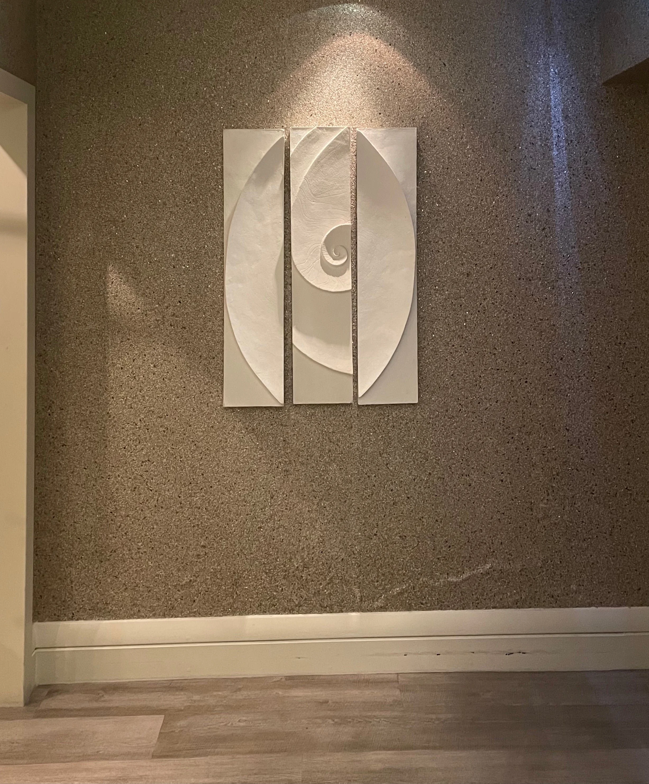 Shellwave Between Two Concave Moons wall sculpture lit on a warm textured wall