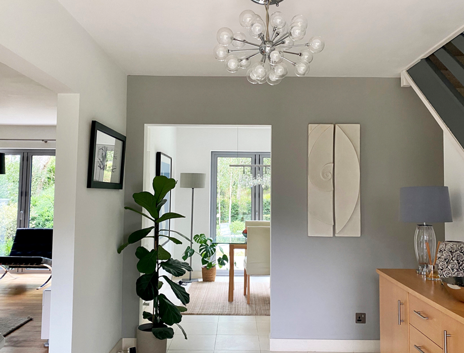 Moon and Shellwave wall sculpture hung in a hallway beside a chandelier and open living space