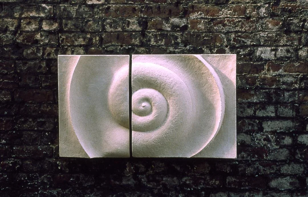 Bone Spiral wall sculpture lit on a dark brick wall, the carved spiral catching pink and violet light