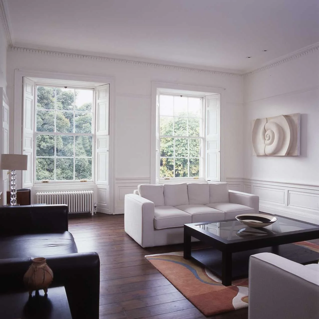 Bone Spiral wall sculpture hung in a bright living room with white sofas and tall sash windows