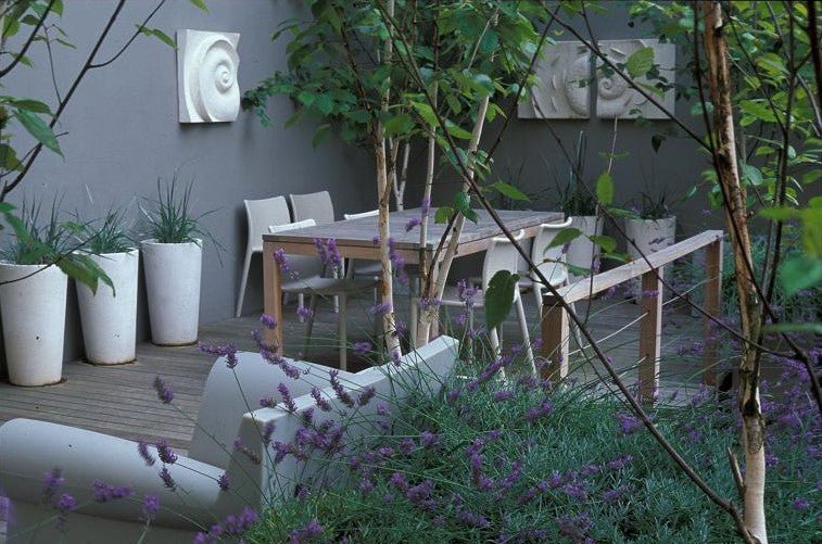 Spiralmoon wall sculpture on the grey wall of a contemporary garden terrace with dining table and lavender
