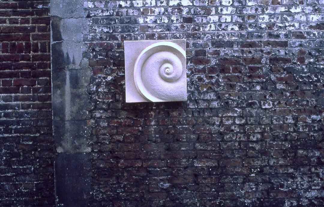 Spiralmoon wall sculpture lit at night on a dark brick wall