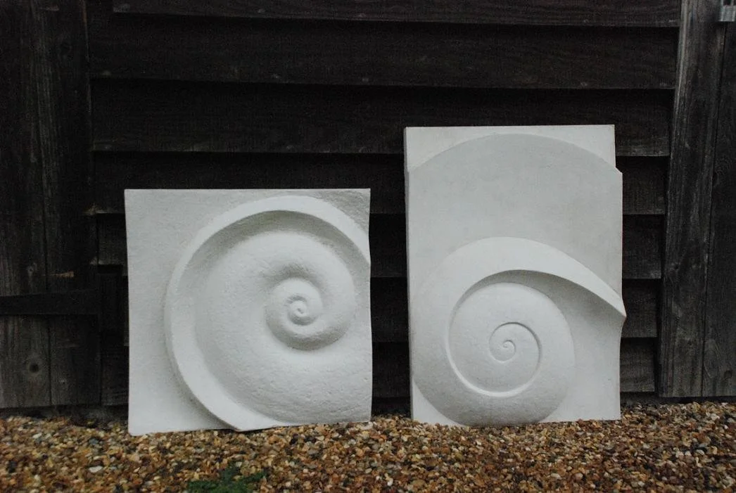 Two Moonspiral wall sculpture panels standing outdoors against weathered timber boarding