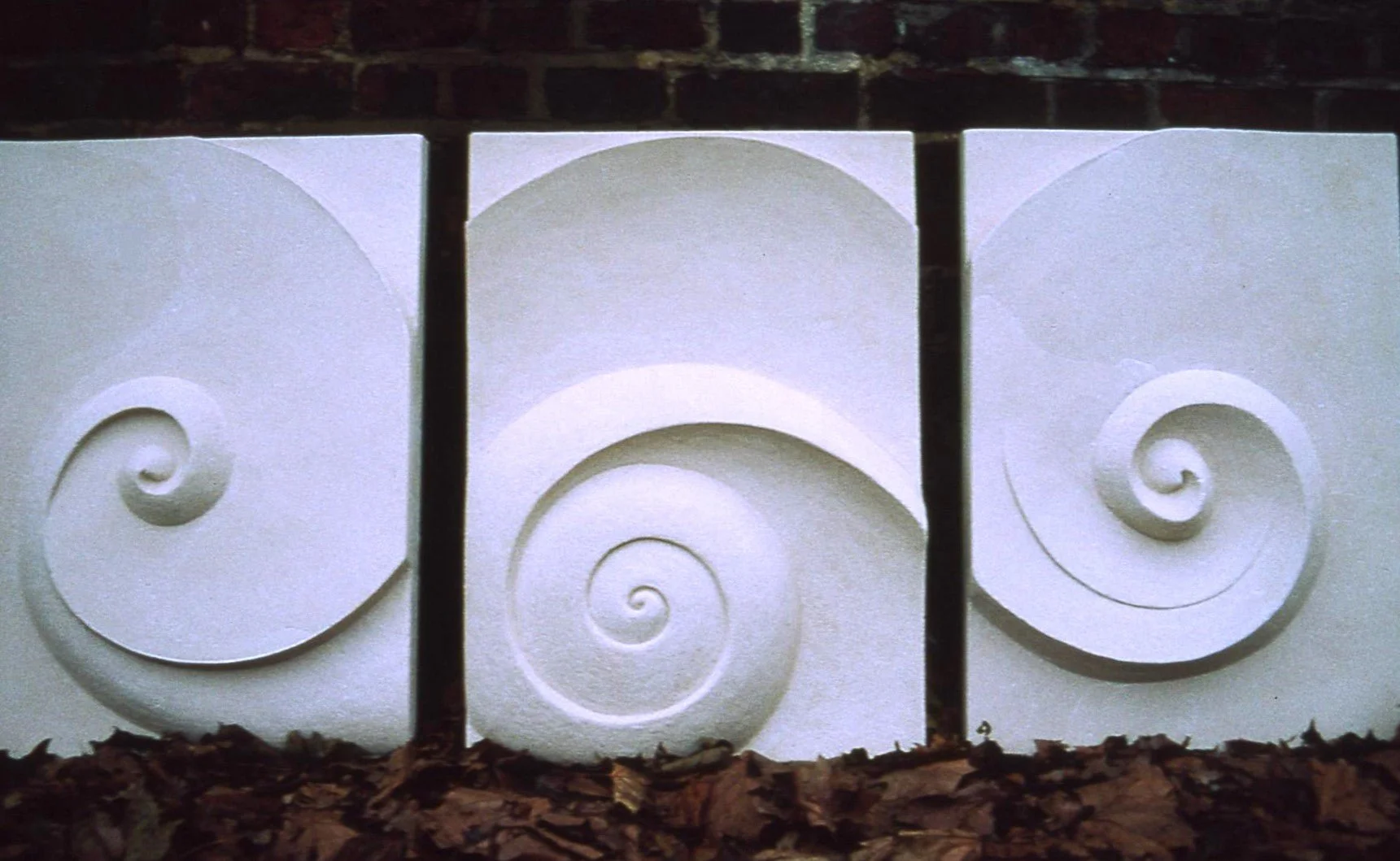 Three Moonspiral wall sculpture panels lit against a dark wall, their spirals reading as a sequence