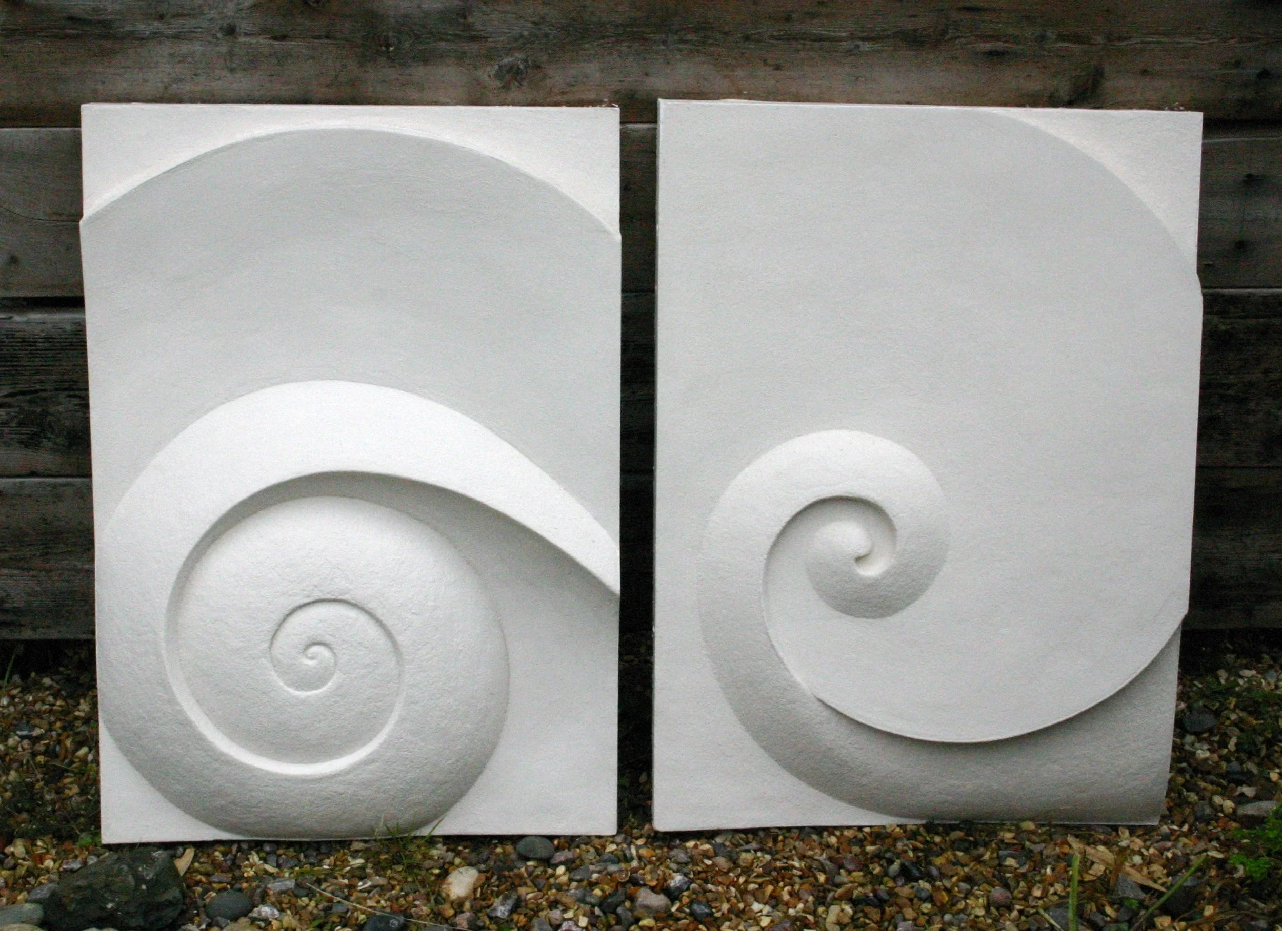 Two Moonspiral panels standing side by side outdoors, showing the mirrored carved spirals