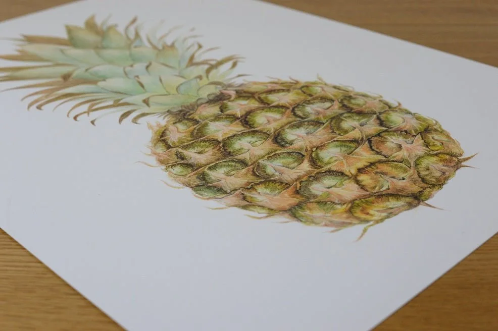 The Pineapple Portrait watercolour print lying at an angle on a wooden table