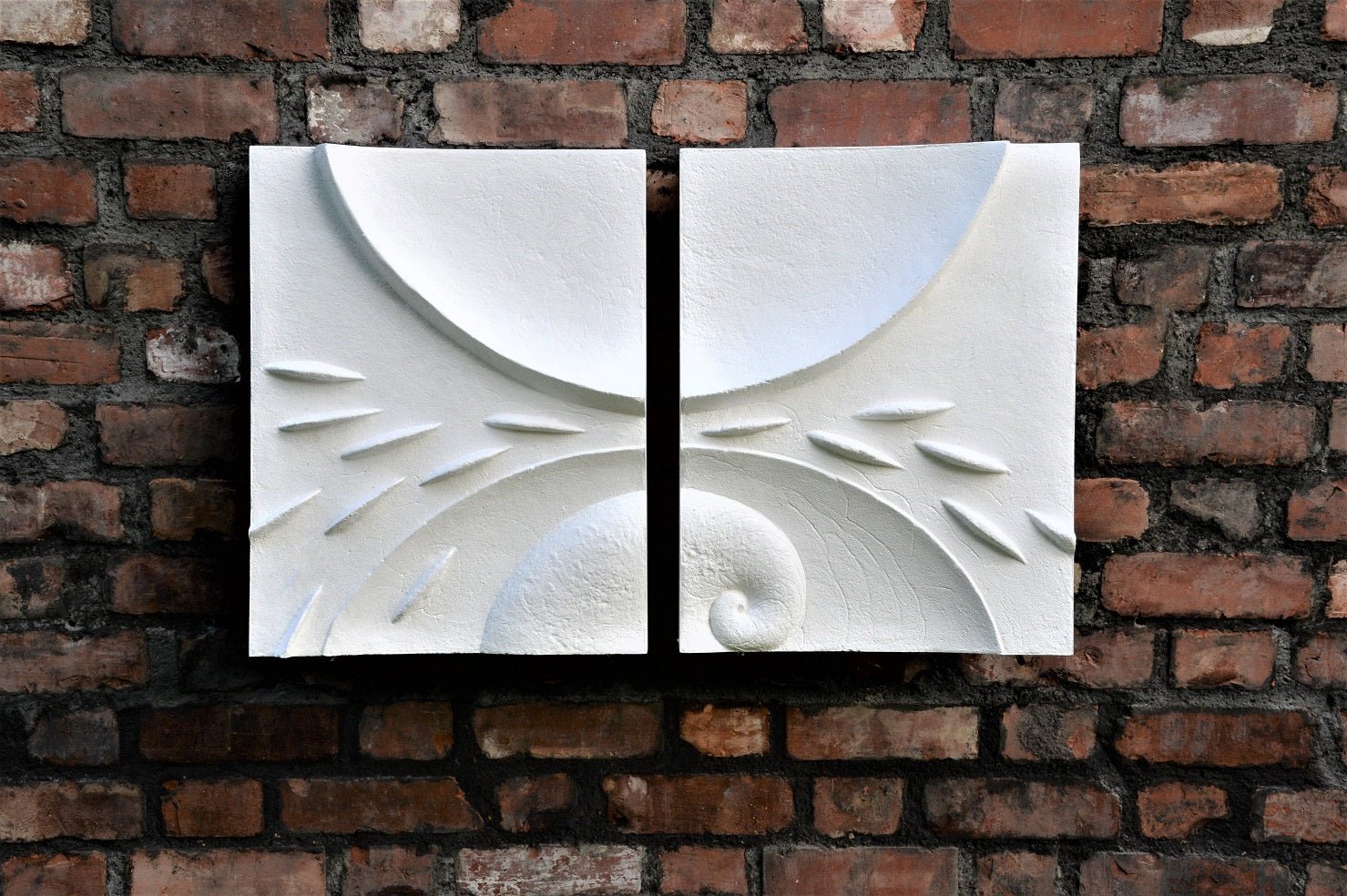 Moon Fishwave wall sculpture, a two-part white carved relief of fin and wave forms mounted on red brick