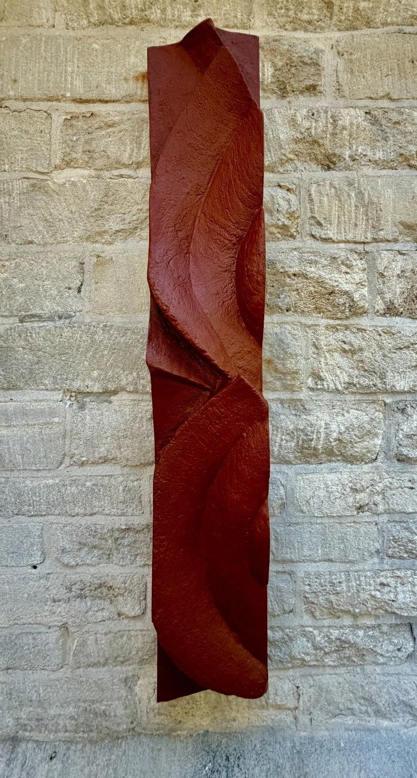 Frozen Deco wall sculpture in terracotta-effect gypsum composite, a tall twisting ribbon form on a pale stone wall