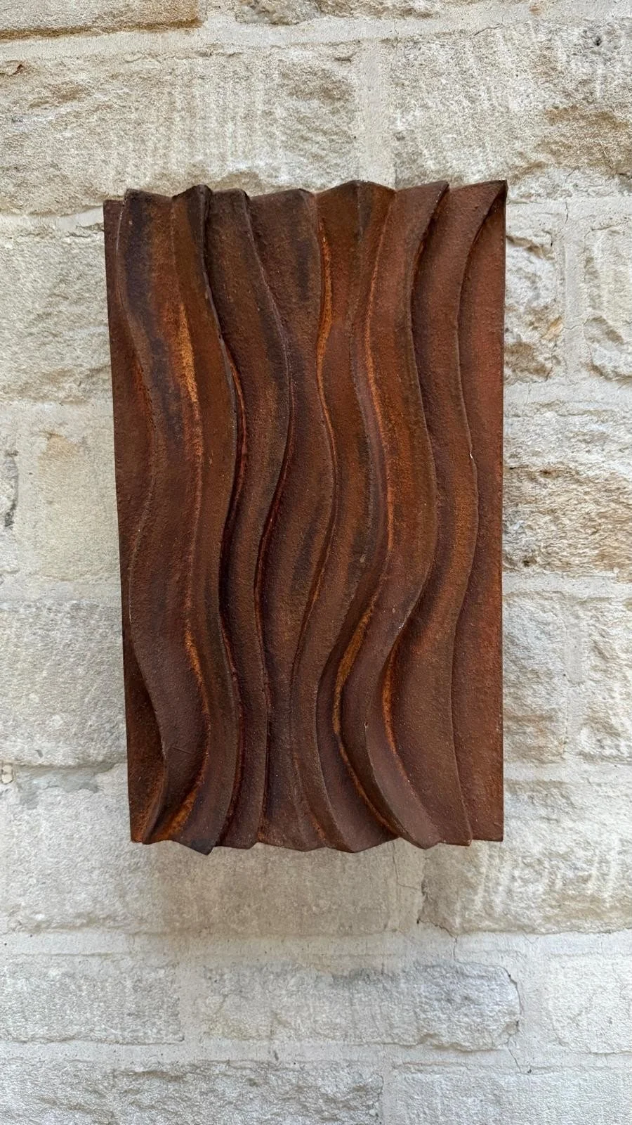 Wall sculpture with a carved wave relief and hand-painted faux rust finish, hung on a pale stone wall