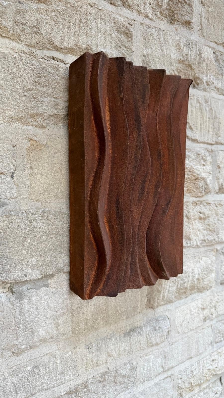 Angled view of the faux rust wave relief wall sculpture showing the depth of its carved waves