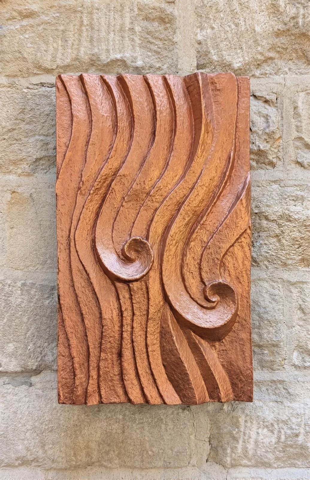 Wall sculpture with a carved wave relief and hand-laid copper surface, hung on a pale stone wall