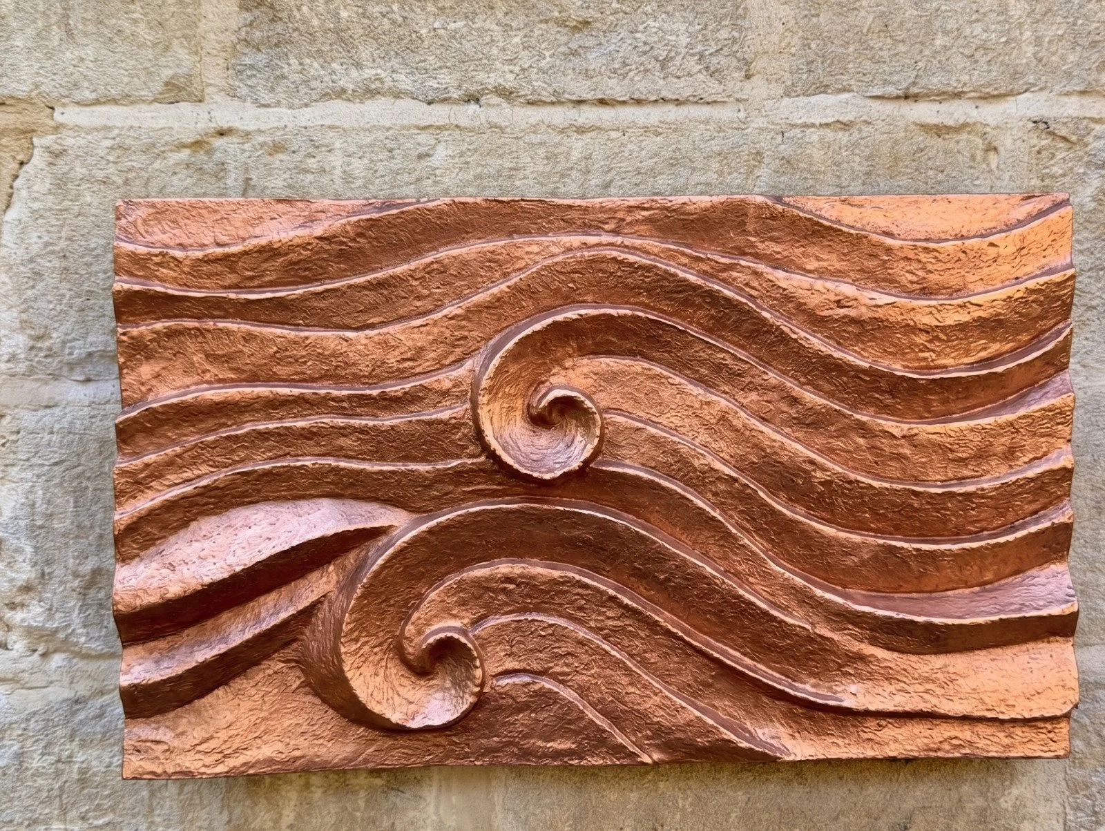 Copper-surfaced wave relief wall sculpture hung horizontally, its carved waves curling into two spiral scrolls