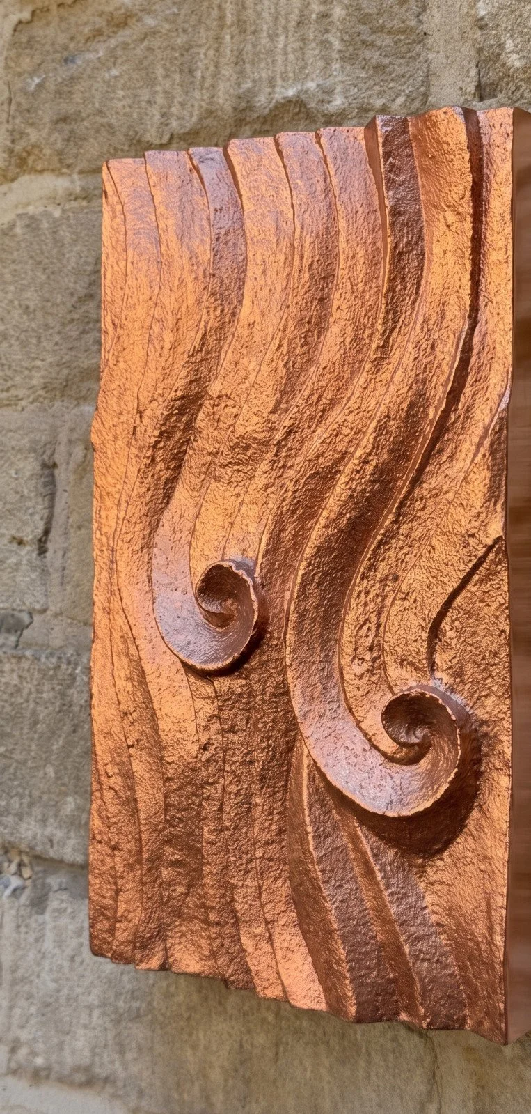 Close view of the hand-laid copper surface on the wave relief wall sculpture, showing its warm patina and spiral scroll