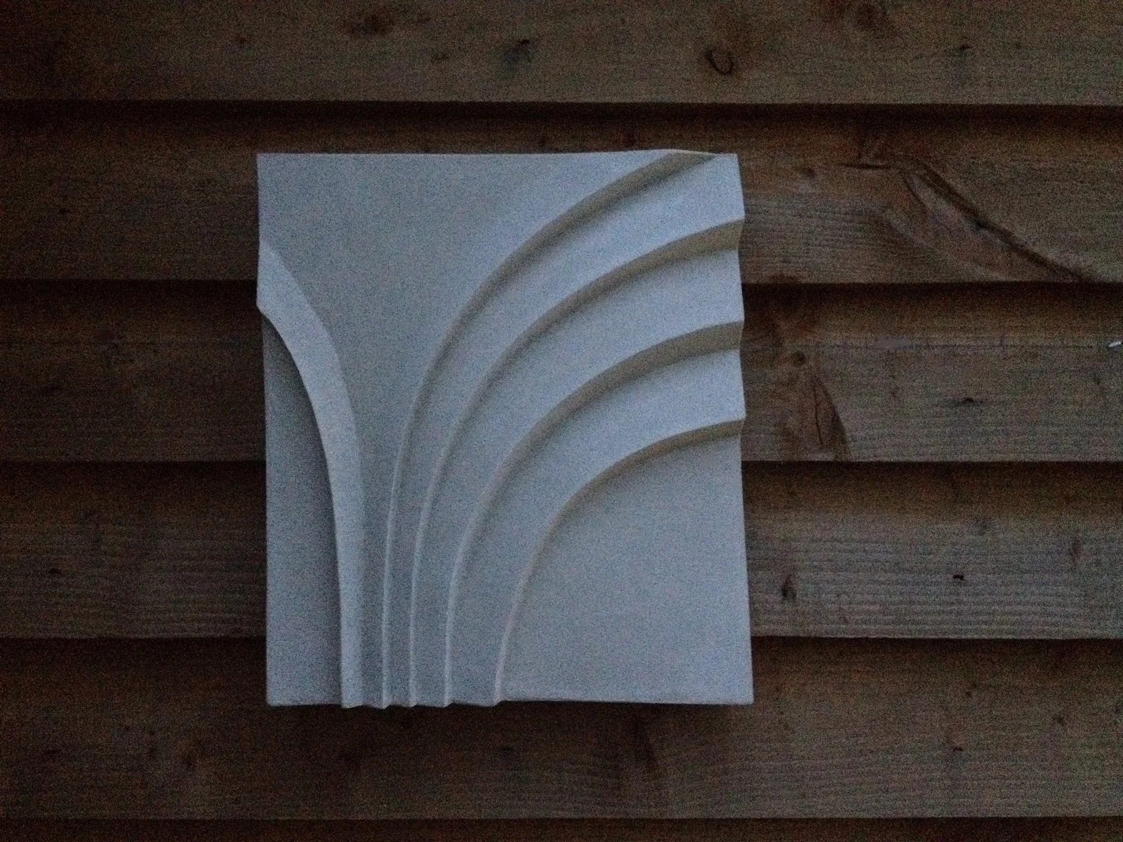 Palm Form One wall sculpture, a stone-finish panel carved with a sweeping fan of palm frond ribs, on timber cladding
