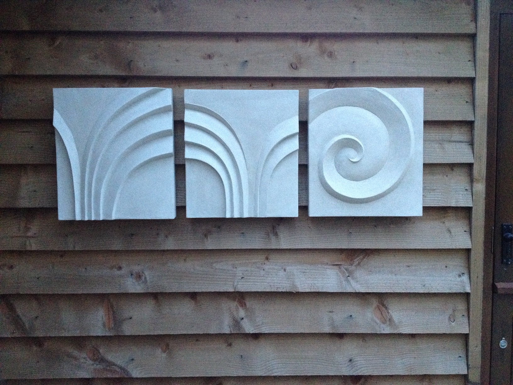Two Palm Forms with Spiral wall sculpture shown as three separate carved panels spaced across a timber wall