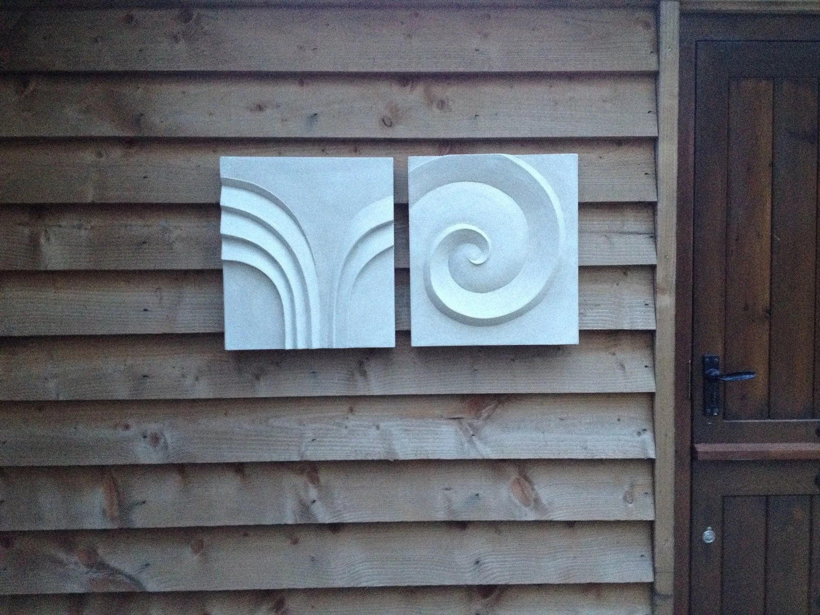 Spiral of Palm Form wall sculpture, a two-part relief pairing a carved palm frond with a spiral, on timber cladding