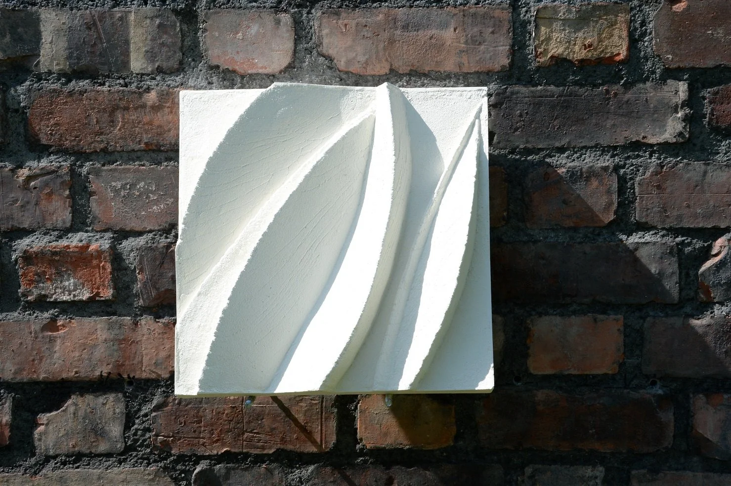 Leaf Form wall sculpture, a white stone-finish relief of slender carved leaf shapes, mounted on a brick wall