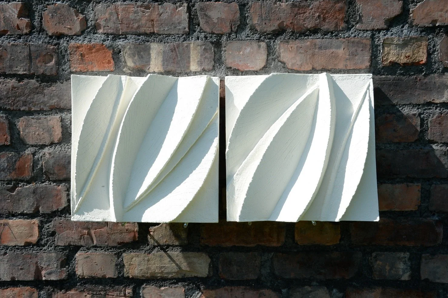 Two Leaf Form wall sculpture panels hung side by side on a brick wall, carved leaf reliefs meeting across the join