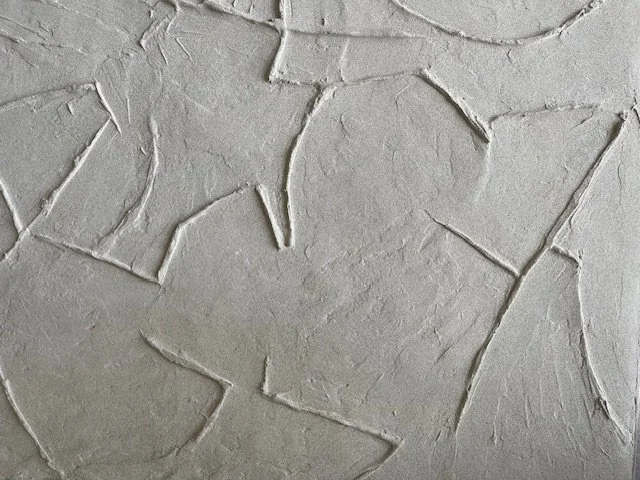 Close-up of the white Icarus relief, showing intersecting angular lines and a rough textured surface.