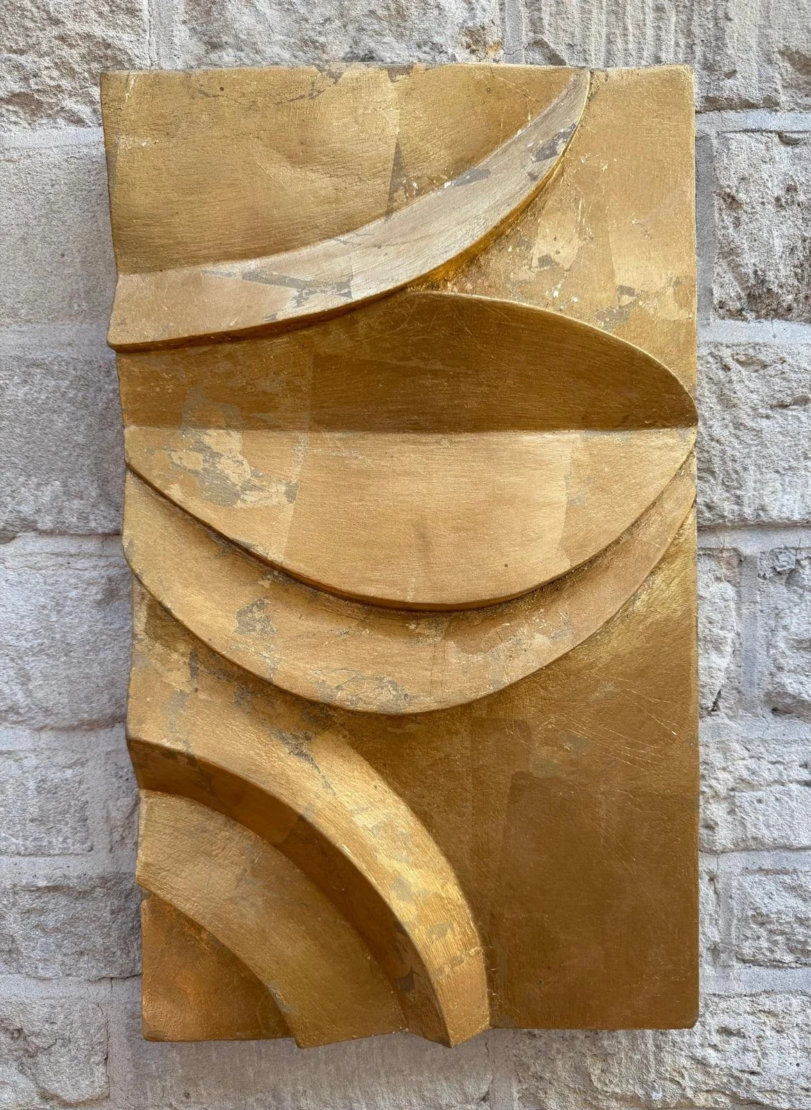 Gold-coloured curved relief panel on a stone wall, with shadows beneath the raised arcs.