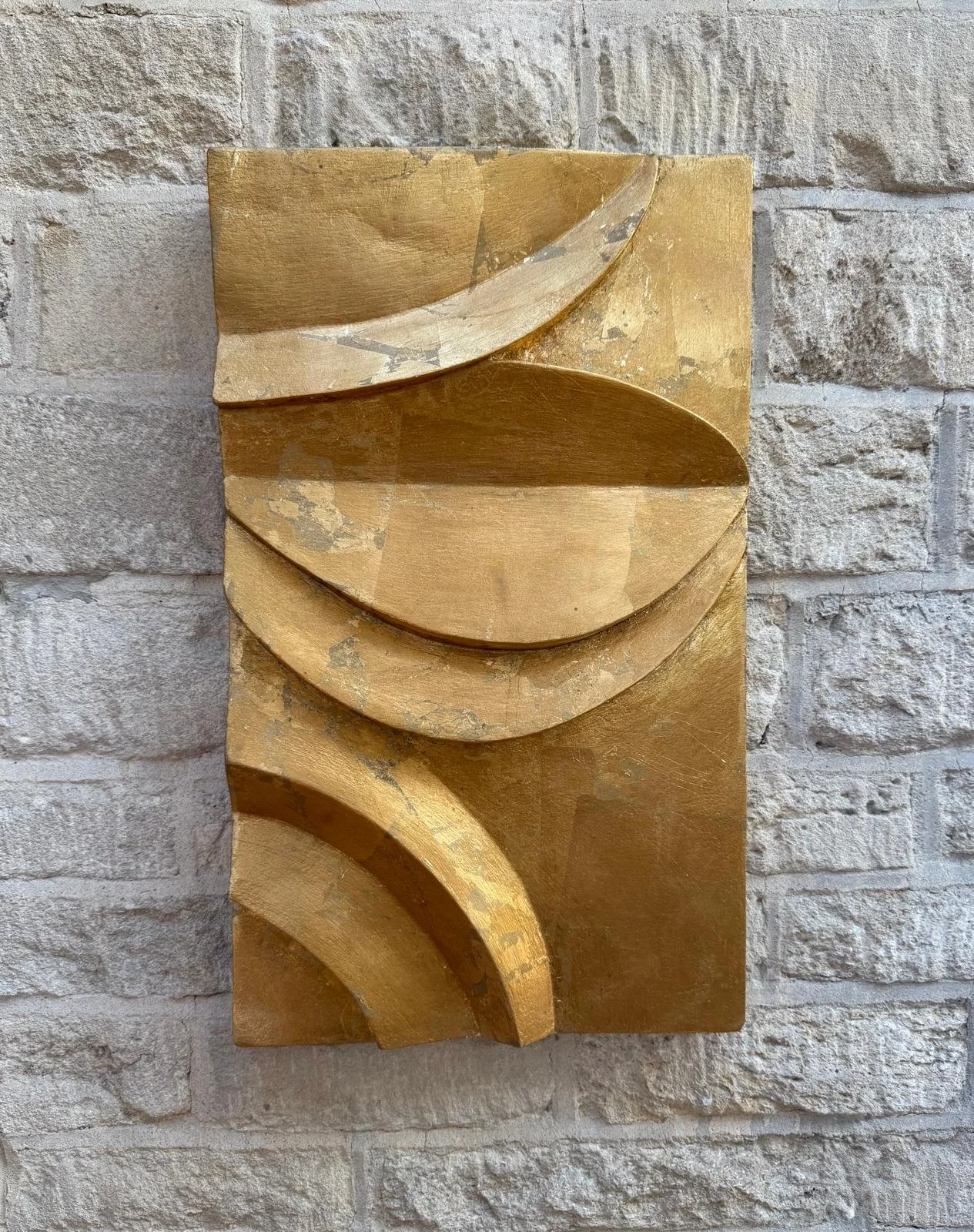 Angled view of a gold-coloured rectangular relief with overlapping curved bands on a stone wall.