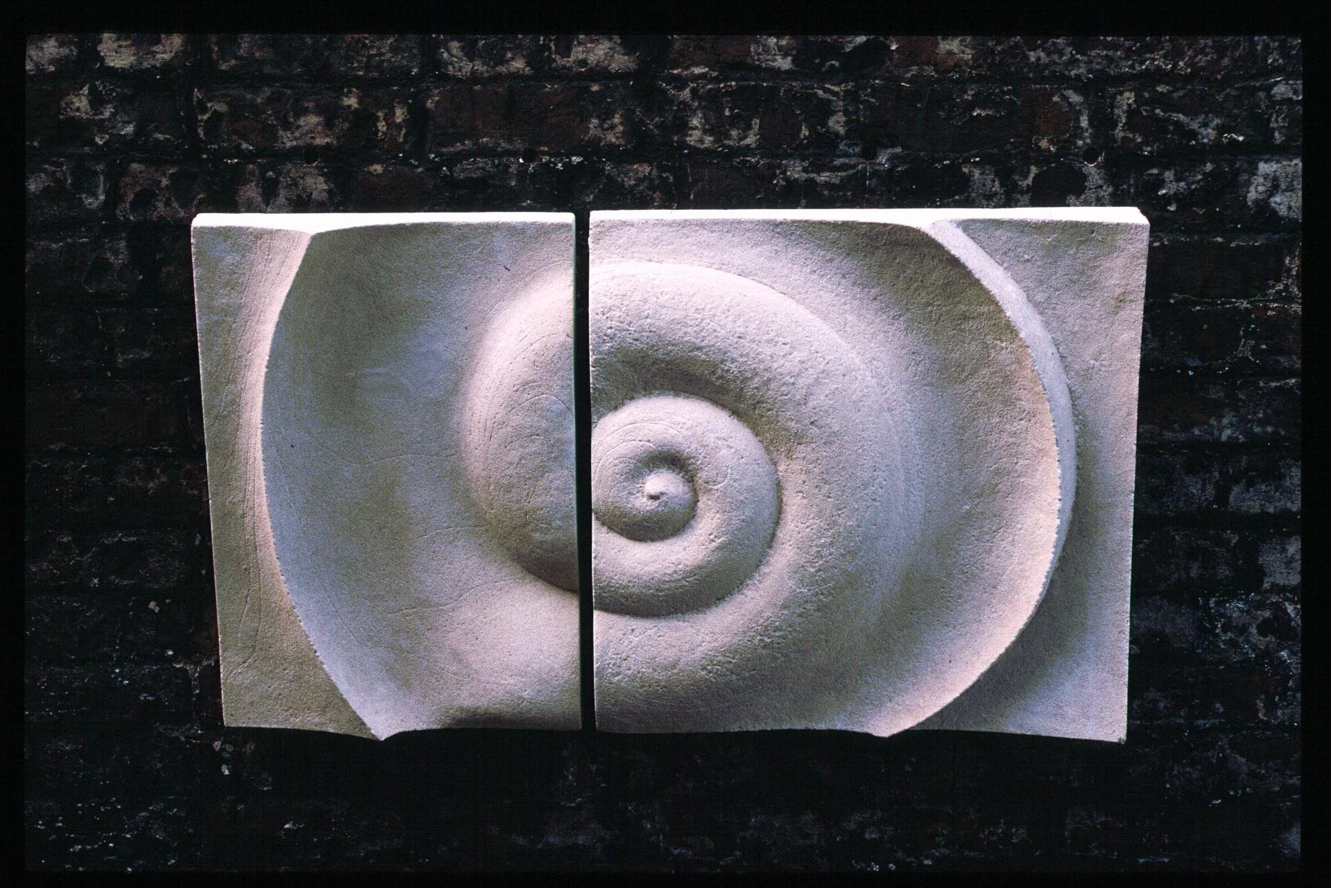 Two white Bone Spiral panels on a dark brick wall, forming a spiral across the central join.