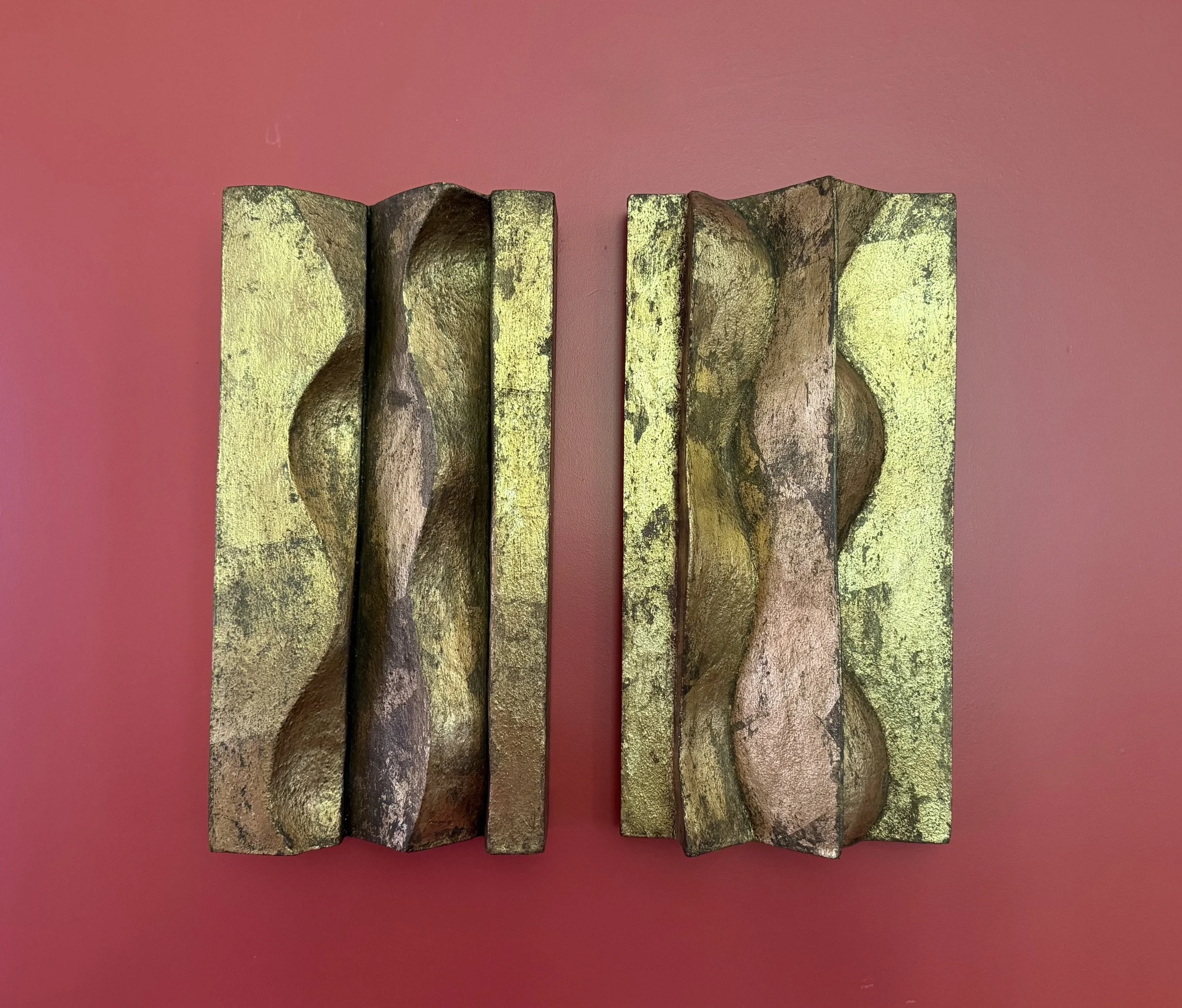 Paired Brancusi relief panels with gold-coloured and dark wavy surfaces against a red background.