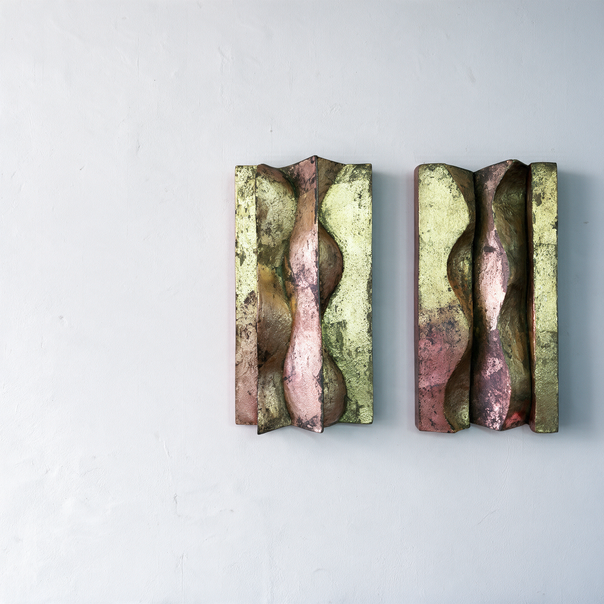 Two Brancusi relief panels with wavy vertical forms and mottled gold, brown and dark surfaces on a pale wall.