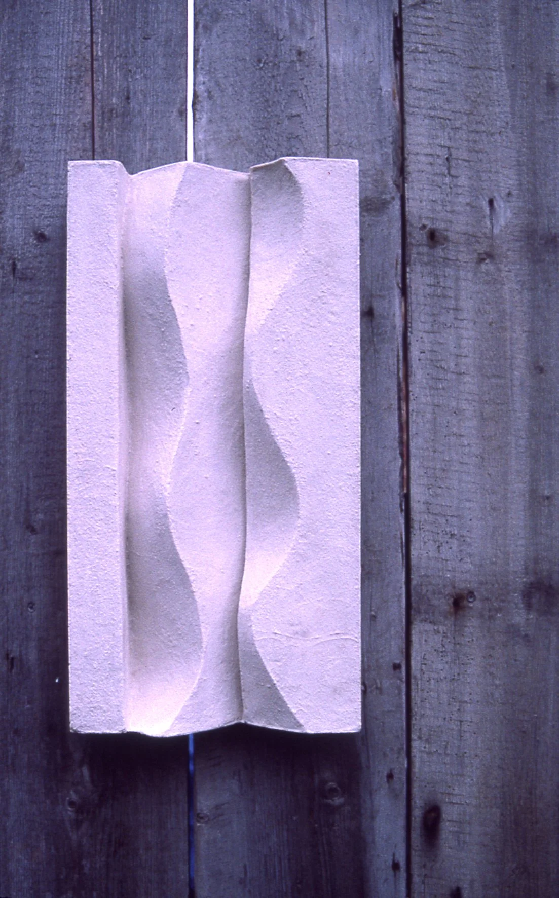 White Brancusi 1 relief mounted vertically on timber, with light defining its wavy recess.