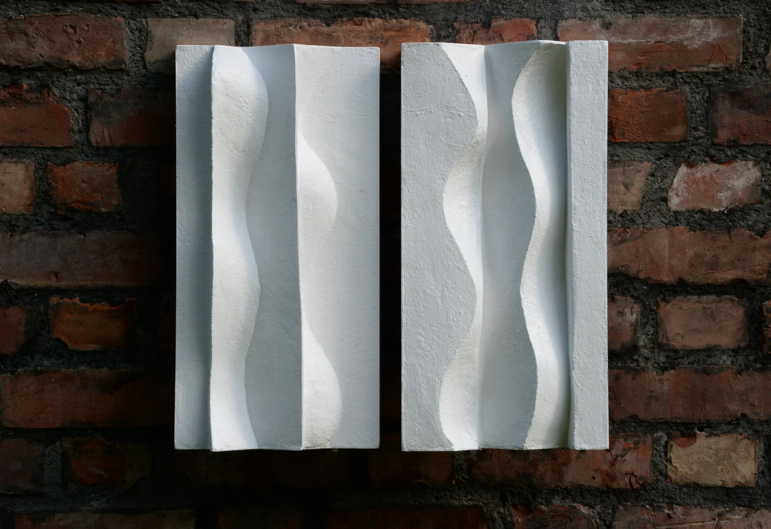 White Brancusi diptych shown straight on against a brick wall.